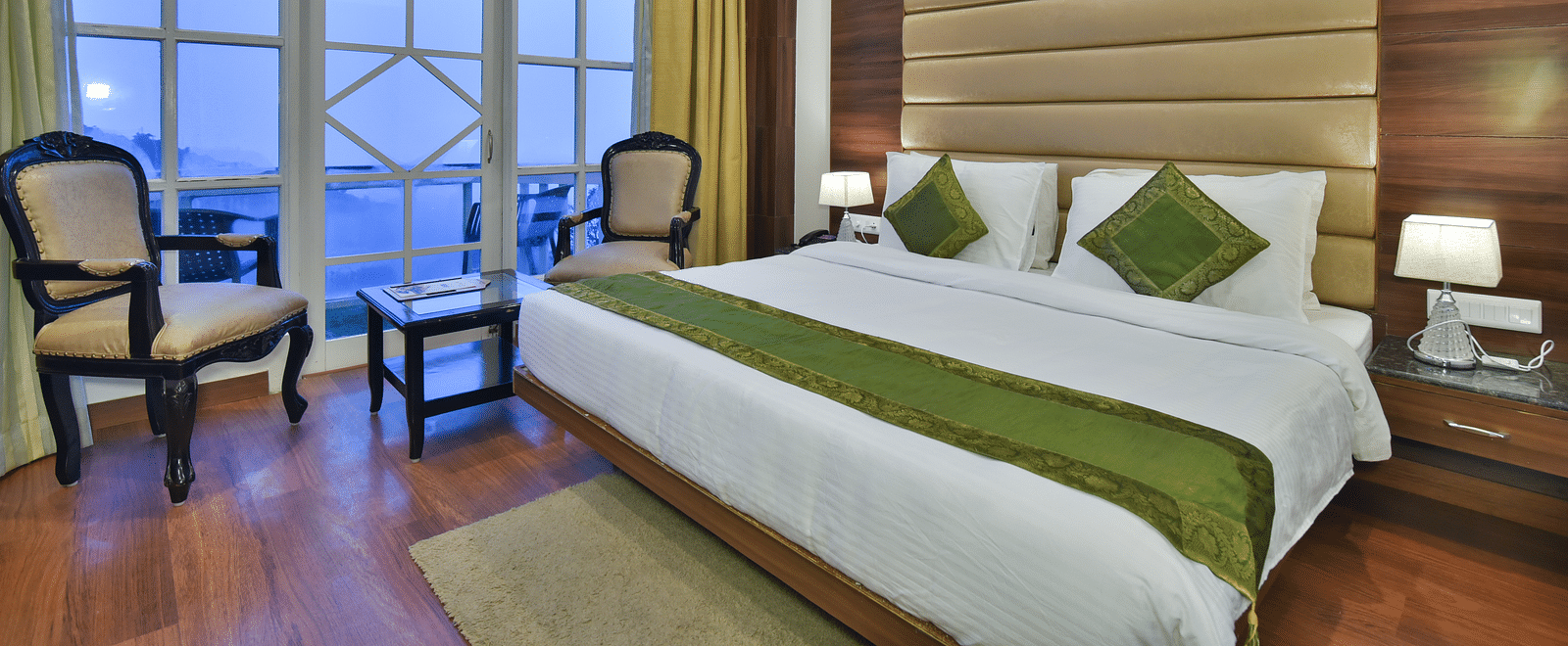 A large bed next to two chairs placed near a large window in the Premium Room at DLS Highland Resort and Spa, Mussoorie.